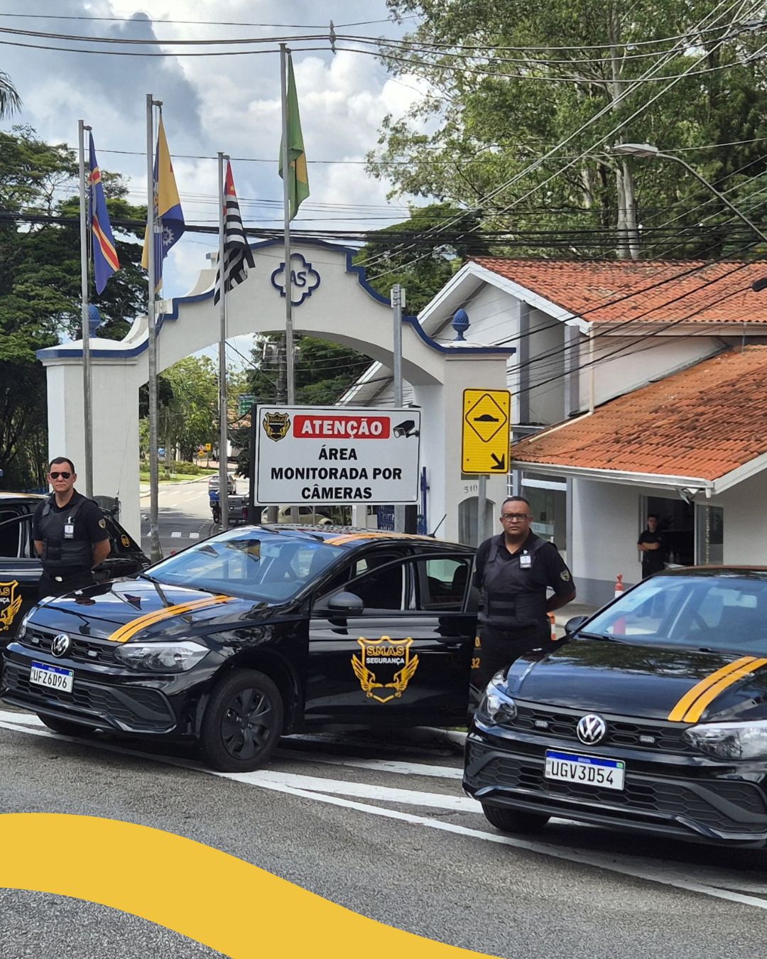 Esta imagem mostra dois carros de segurança pretos, modelo Volkswagen Polo, com faixas amarelas e o logotipo da SELAS Segurança nas portas e no capô [1, 2]. Os veículos estão posicionados em frente a um portal branco com detalhes em azul, onde se lê "AS" em um emblema central.