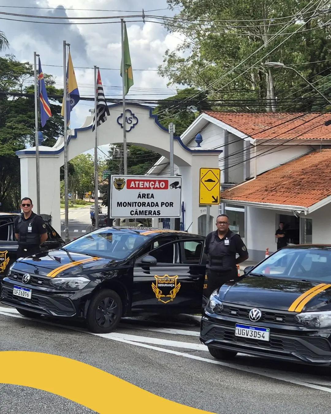 Esta imagem mostra dois carros de segurança pretos, modelo Volkswagen Polo, com faixas amarelas e o logotipo da SELAS Segurança nas portas e no capô [1, 2]. Os veículos estão posicionados em frente a um portal branco com detalhes em azul, onde se lê "AS" em um emblema central.